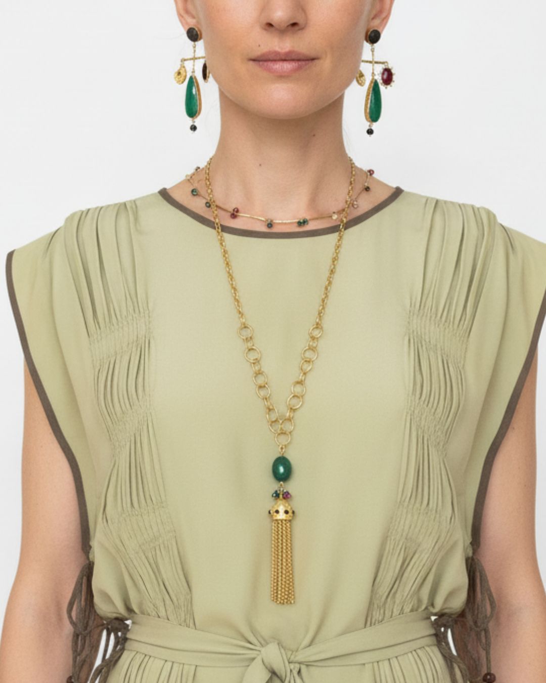 Woman wearing a green dress with statement earrings and a gold choker necklace and pendant tassel, on a white background