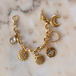 Lanamara Celestial gold charm bracelet flat lay on marble with crescent moon, sun and shell charms