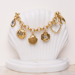 Lanamara Celestial Charm Bracelet displayed on a shell stand, gold sun, shell, rose and heart charms