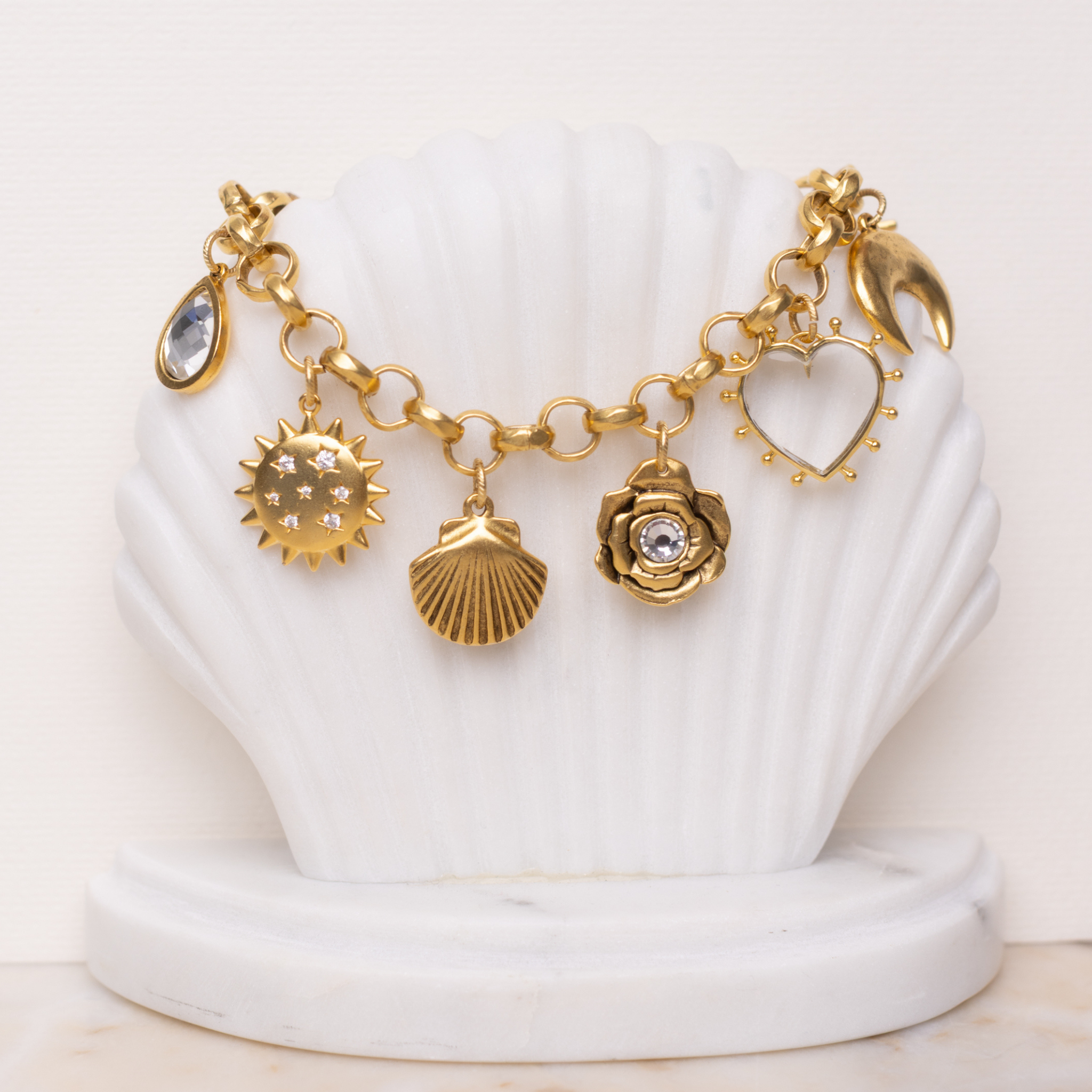 Lanamara Celestial Charm Bracelet displayed on a shell stand, gold sun, shell, rose and heart charms