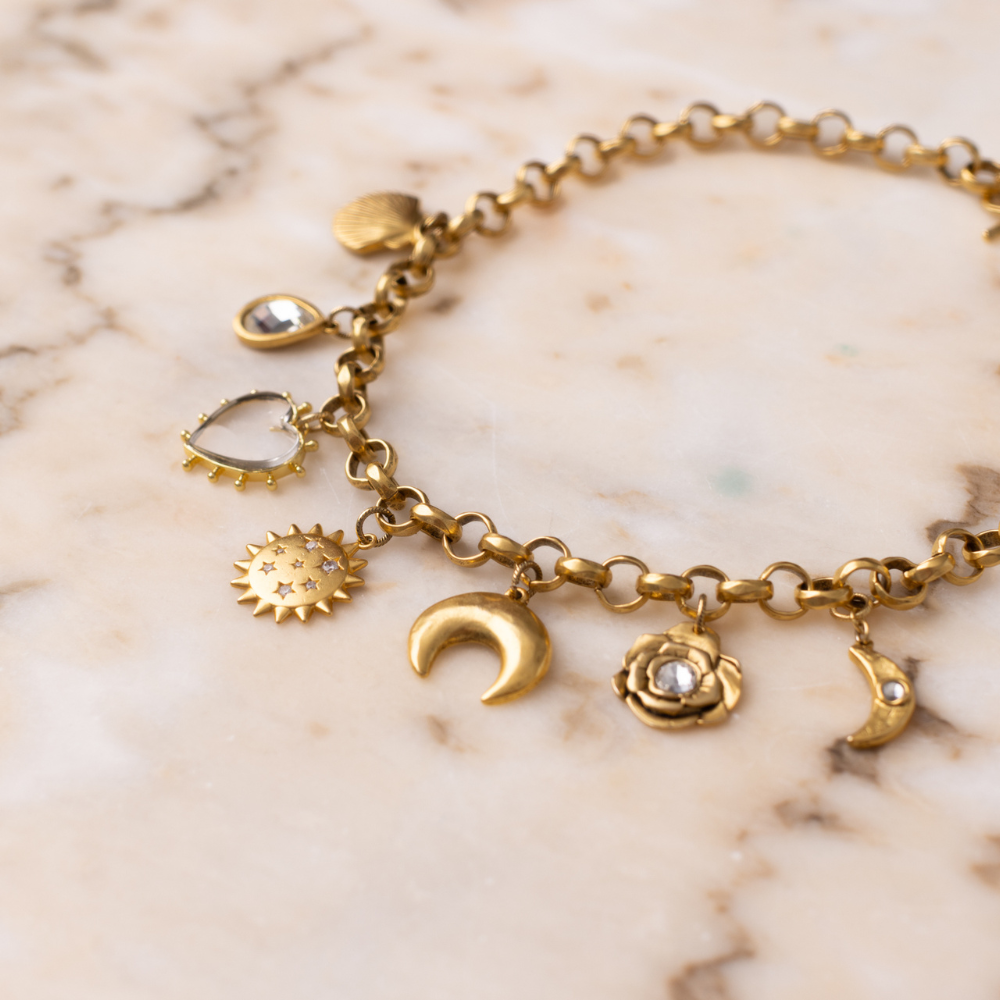 Gold Celestial Charm Necklace styled on marble, showing sunstar, crescent moon and rose charms
