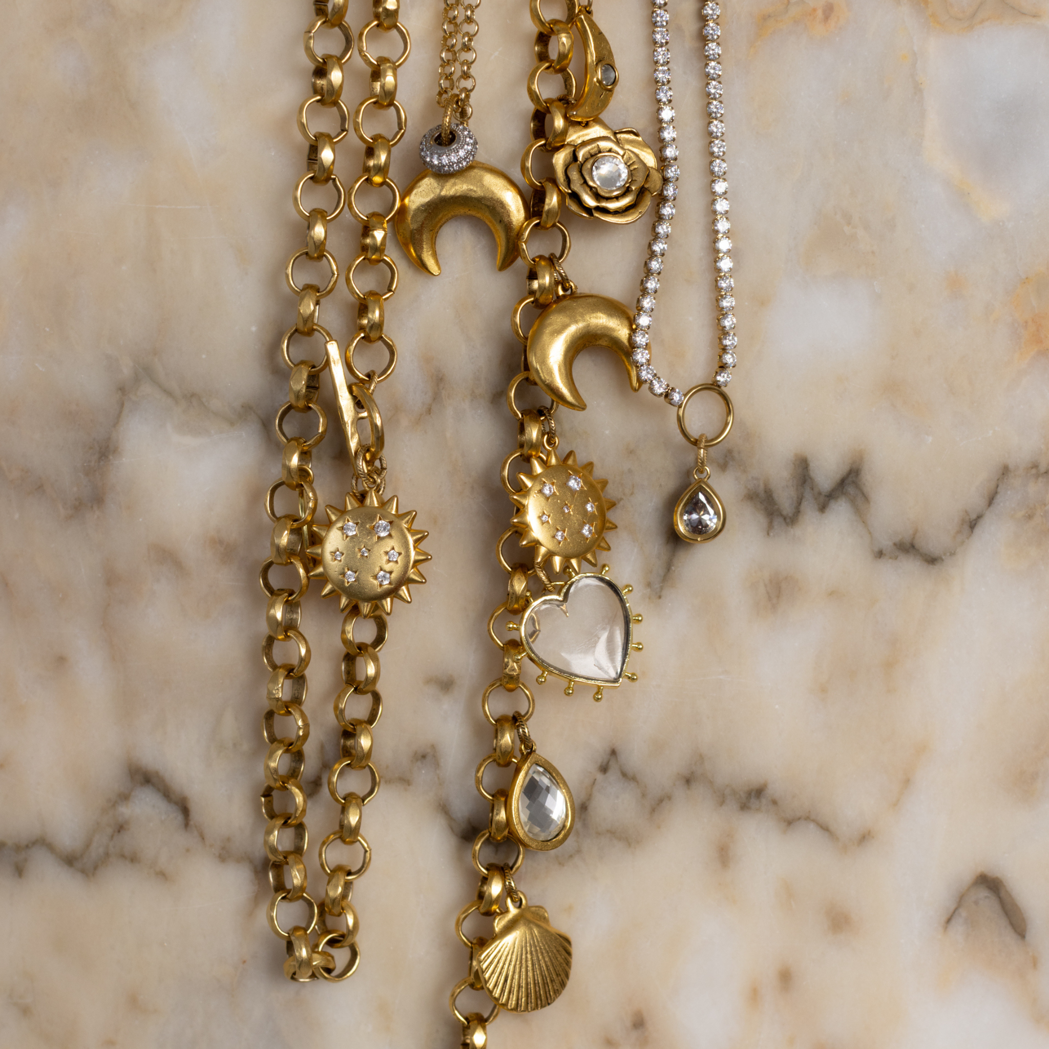Lanamara Celestial jewellery styled on marble — gold charm necklace with sunstar, crescent moon and clear quartz heart charms