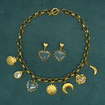 Lanamara Celestial collection flatlay with a gold charm necklace and Open Hearted clear quartz heart earrings on a deep green background