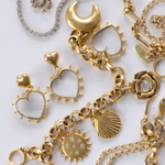Close-up flatlay of Lanamara Celestial charms including open heart earrings, moon, sun, shell and rose on white fabric