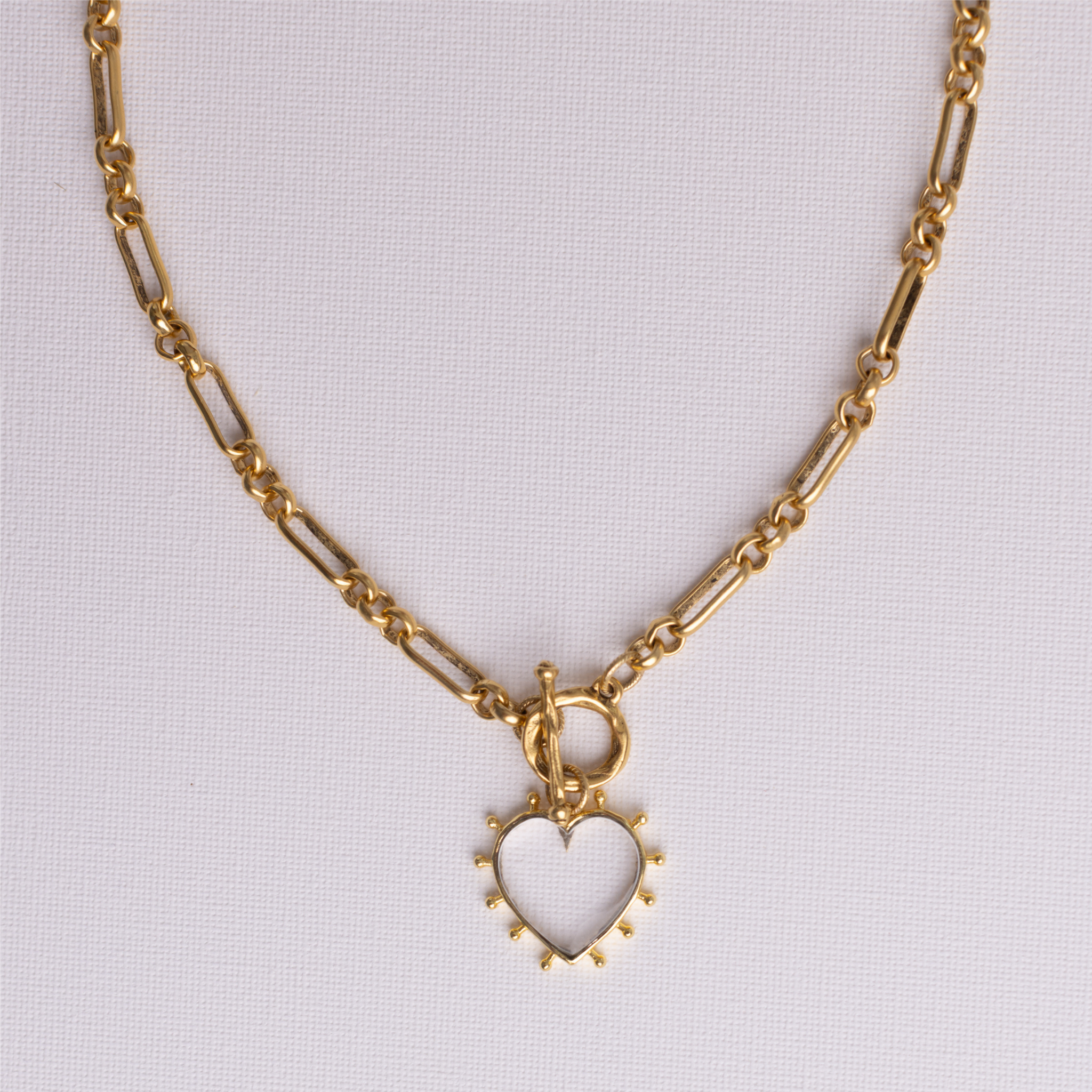 Clear quartz open heart pendant and front toggle clasp on gold heirloom chain, flat lay