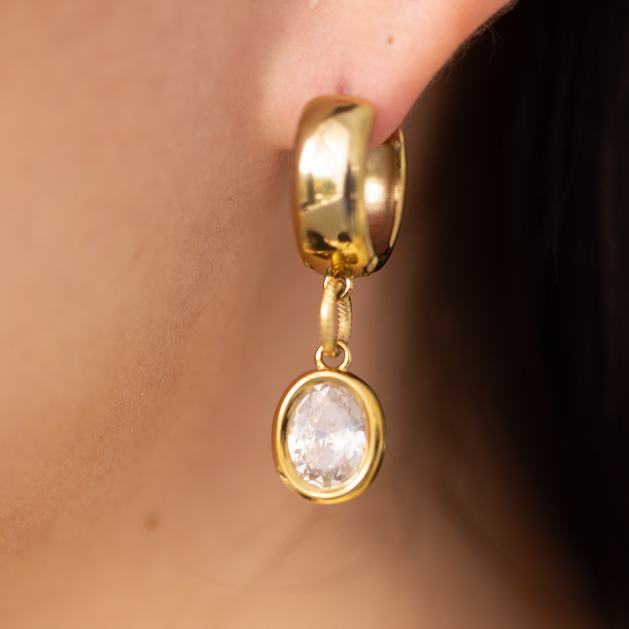Close-up of Lanamara gold huggie earring with bezel-set oval CZ drop