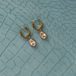 Lanamara Vintage Clarity oval CZ huggie earrings, flat lay on teal