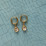 Lanamara Vintage Clarity pear CZ huggie earrings, flat lay on teal